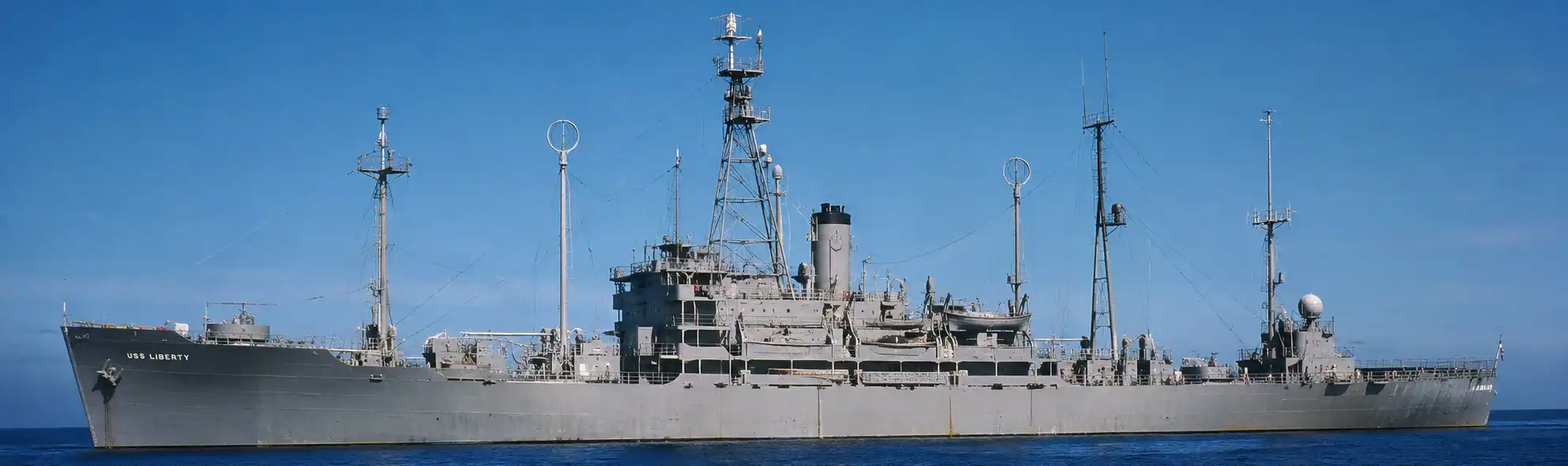 A historically inspired panoramic illustration of the USS Liberty (AGTR-5) sailing peacefully through calm Mediterranean waters before the 1967 attack, showing the intelligence ship in pristine condition beneath a clear blue sky with her distinctive antennas, superstructure, and American naval markings clearly visible.