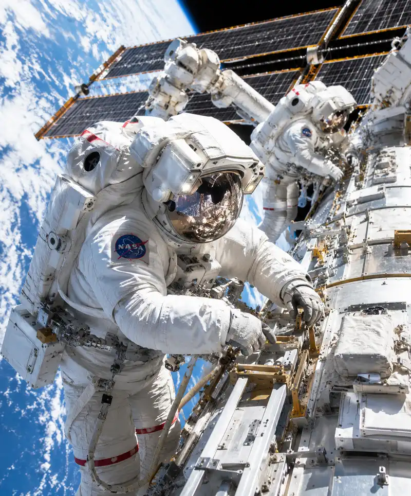 Two astronauts perform a spacewalk outside a modern space station, working on advanced equipment high above Earth in a bright and dramatic scene of modern space exploration.