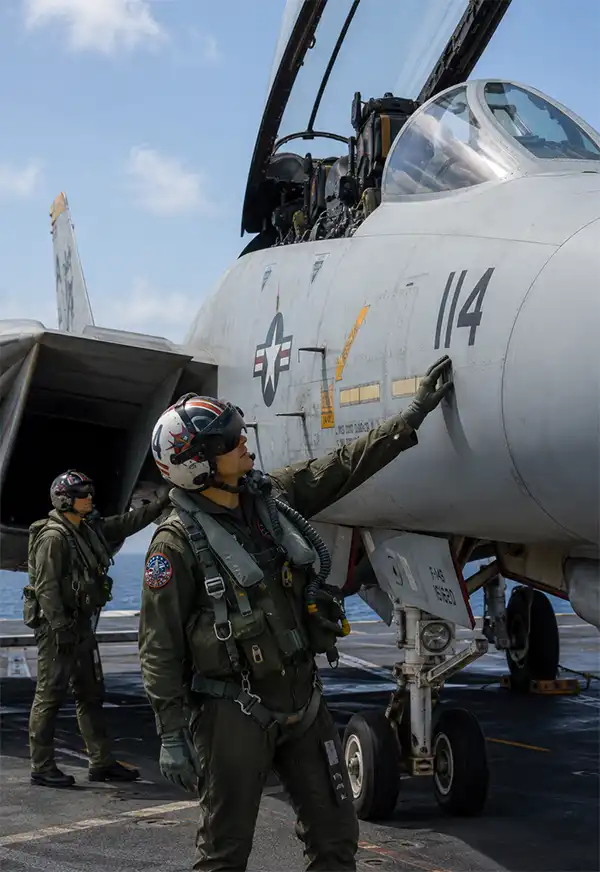 Preflight Checks A U.S. Navy pilot and his radar intercept officer perform a meticulous pre-flight inspection of an F-14 Tomcat on the deck of an aircraft carrier. With the cockpit canopy raised and the ocean stretching to the horizon behind them, the two aviators carefully examine the aircraft before preparing for another high-speed mission.
