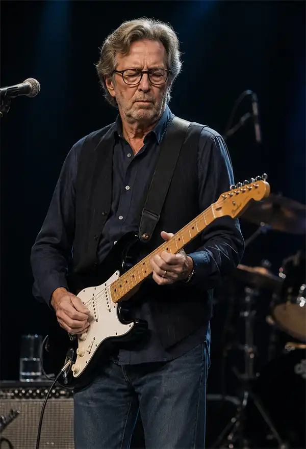 An experienced guitarist performs on stage with an electric guitar under concert lighting, delivering a soulful live performance as drums and stage equipment fade into the background.